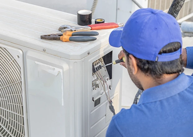 Technician servicing an outdoor air conditioner with tools nearby