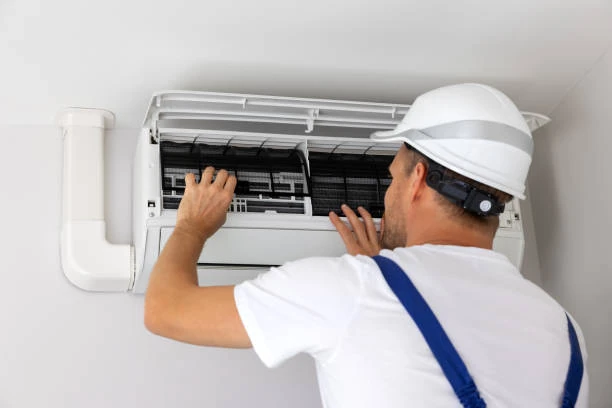 Technician in a hard hat inspecting a wall-mounted air conditioner